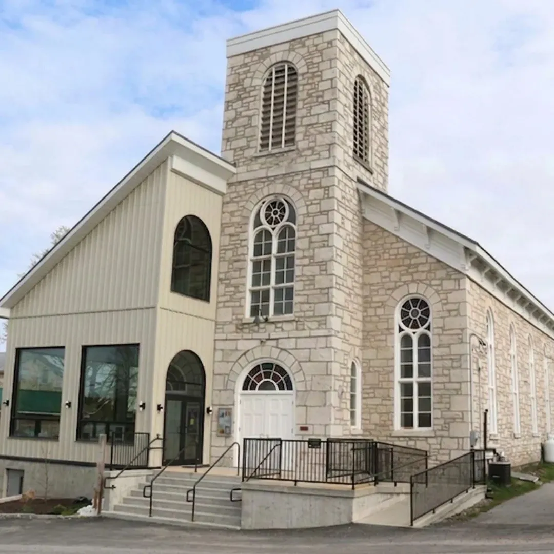 The Marble Arts Centre, a limestone church with a square bell tower and round-arched windows, joined on the left by a new glass-fronted atrium in pale siding