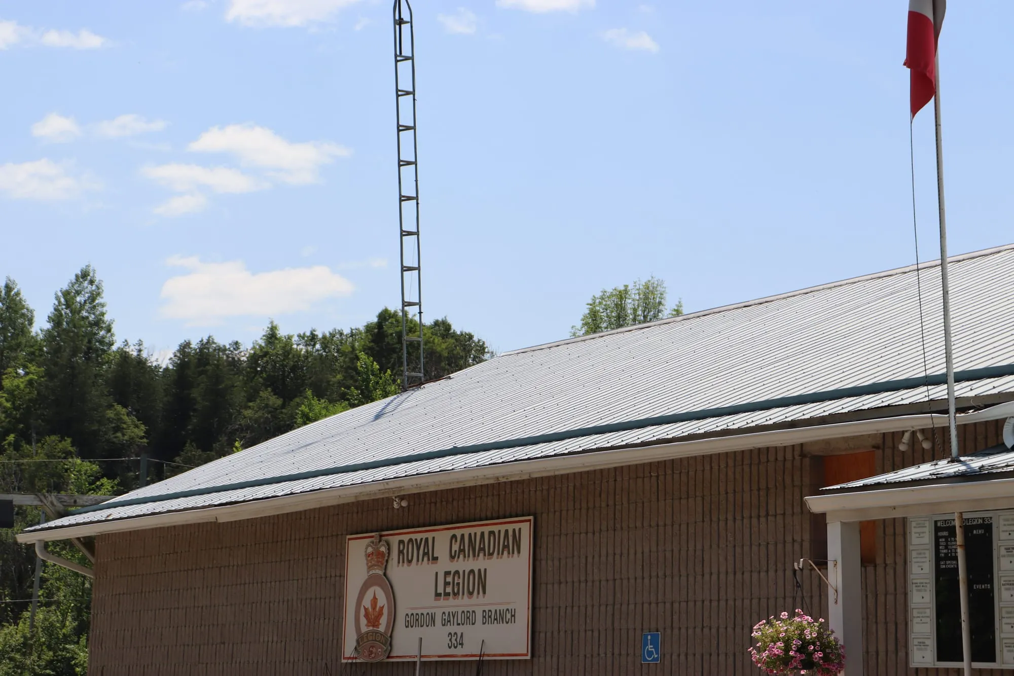 The front of Arden Legion Branch 334, a brown hall with its Royal Canadian Legion sign under the eaves and a radio mast behind