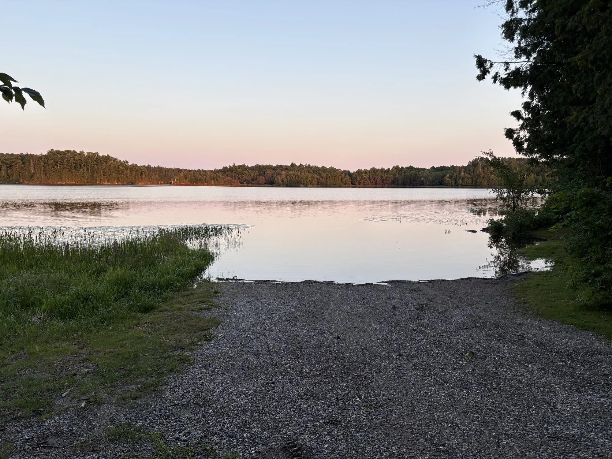 A gravel ramp running into the still water of Bull Lake at dusk, the far shore lit pink