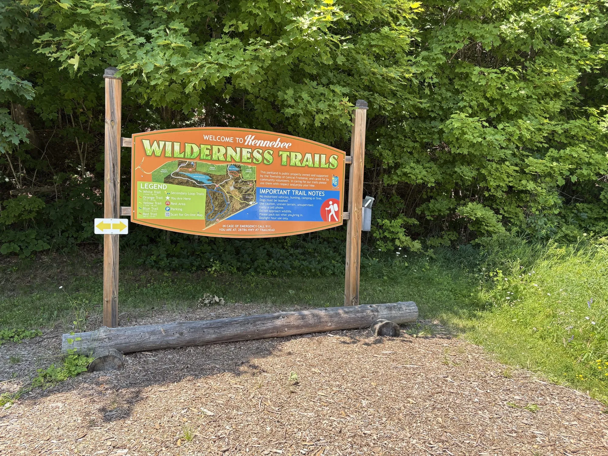 The Welcome to Kennebec Wilderness Trails sign, a painted trail map on two posts, at the gravel trailhead off Highway 7