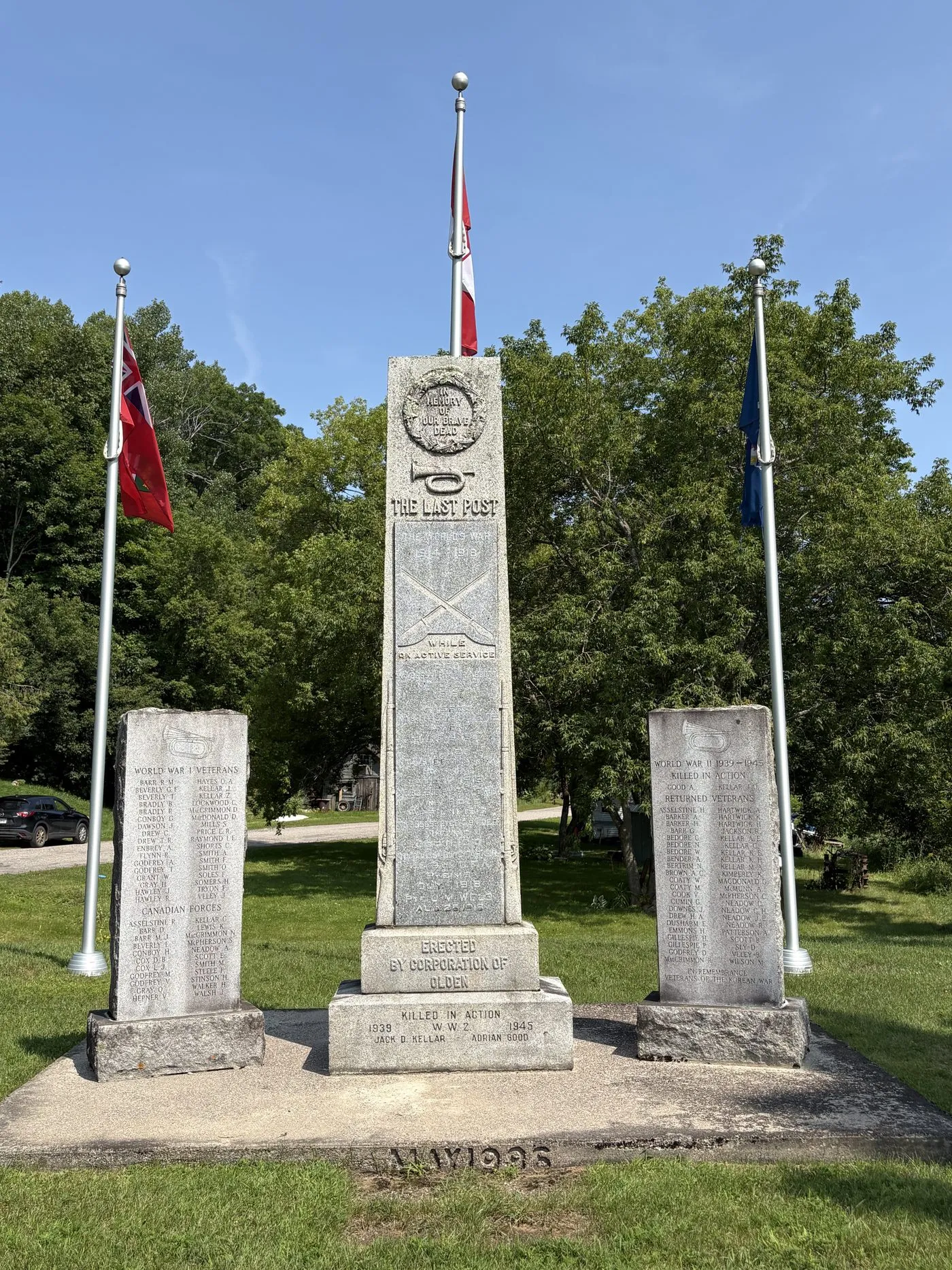 The Olden war memorial at Mountain Grove: a granite column cut with a bugle and the words The Last Post, flanked by two name stones, with the Canadian flag and the Red Ensign flying behind.