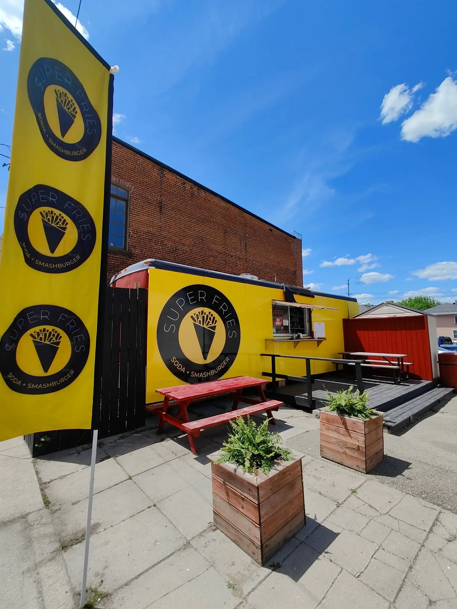 The Superfries trailer in yellow with its Super Fries soda and smashburger logo, an order window, and red picnic tables on the patio