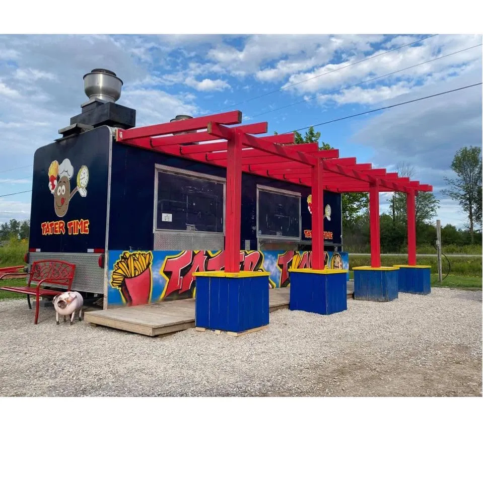 The Tater Time truck in navy and red, a timber pergola over blue and yellow planters, with a pig standing by the bench