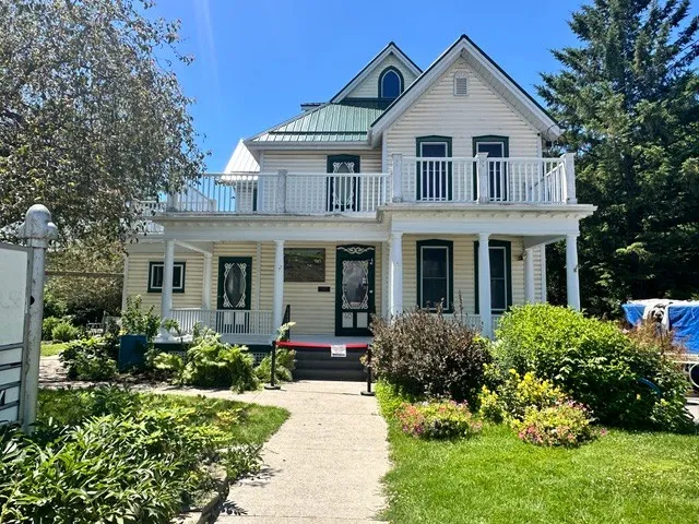 The Heritage Centre, a cream clapboard house with green trim, a wraparound veranda and balcony, gardens along the front walk
